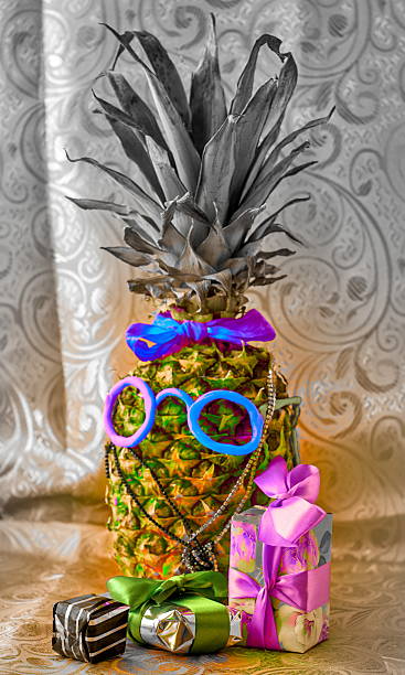 A fresh pineapple is decorated as a funny character with colorful, quirky sunglasses and a costume