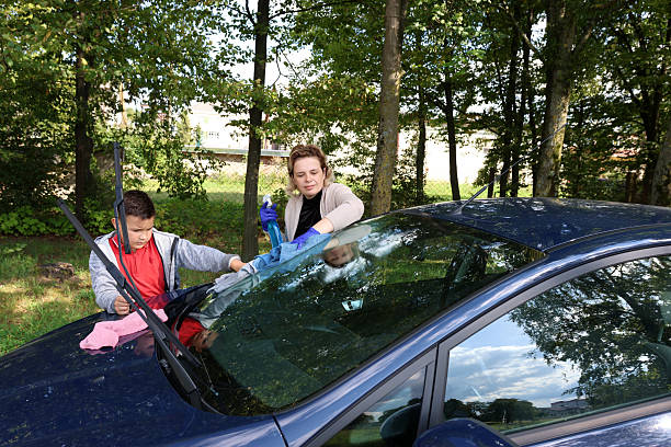 istock Woman and boy clean car window using spray bottle and cloth. 2242432624