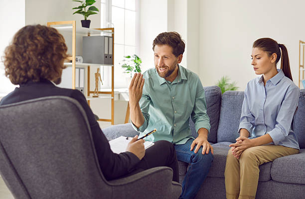 istock Young couple sitting on sofa and talking with psychologist on therapy session. 2242437576