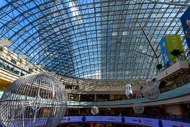 Moscow, Russia - August 27, 2025: Bright sunlight pours through a stunning glass dome, revealing a bustling shopping mall filled with shoppers and elegant decor. The space feels both vibrant and expansive.