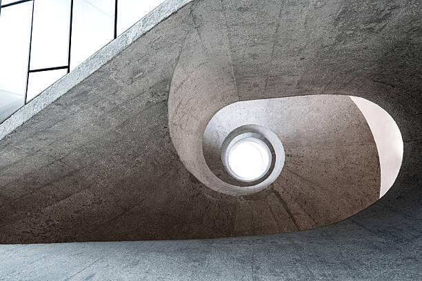 A dramatic spiral concrete staircase forms a circular central opening, guiding the eye toward a bright skylight. Minimalist, industrial architecture emphasizing texture, curve, and space in a stark interior.