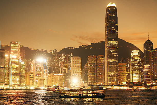 Vibrant Hong Kong skyline at dusk with towering skyscrapers, lit harbor, and a ferris wheel along Victoria Harbour. Captures energetic city life, night light, and maritime activity.