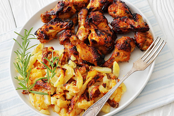 bbq chicken wings with fried potatoes on a plate with rosemary and fork on white wood table, Dutch angle view, not AI generated