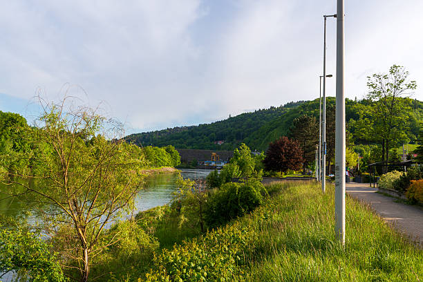 Peaceful riverside path surrounded by vibrant greenery and gentle hills under warm evening light. A calm summer landscape symbolizing relaxation, outdoor recreation, and natural harmony.