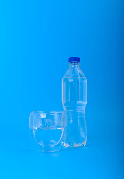 istock Plastic bottle and glass of water on blue background 2242447595