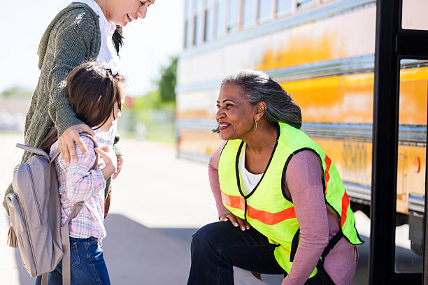 istock Smiling crossing guard helps young student with backpack near school bus. 2242449630