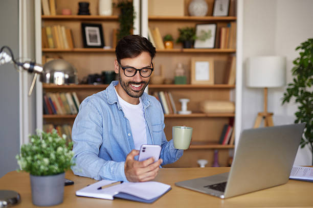 istock Freelancer working from home enjoying a cup of coffee and checking his phone 2242459575