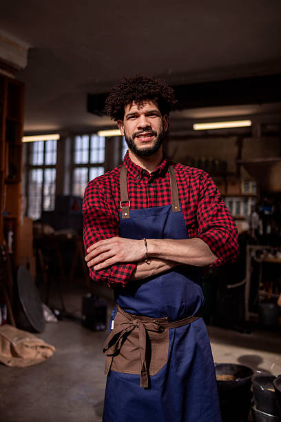 istock Confident Craftsman in Blue Apron Stands Proud in Busy Workshop 2242459880