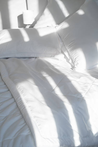 istock A bed with white pillows and a blanket, next to a bedside table with a lamp, daylight 2242460833