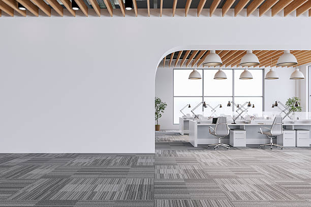 istock Semi-empty office interior with arched white blank wall and copy space,  a wooden slats ceiling, work desks and large windows, on dark gray carpet floor 2242460979
