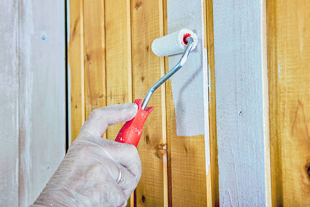 istock Construction worker uses roller to evenly coat wooden panels with white paint. 2242463016