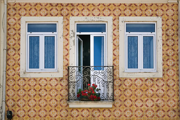 Colorful traditional Portuguese facade with tiled wall, three windows, and a small balcony with red flowers, showcasing classic architecture and ornamental design, horizontal