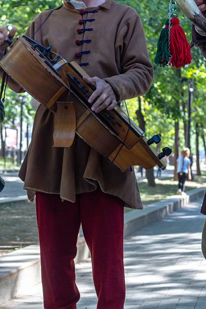 A man in historical costume playing a traditional stringed instrument outdoors during a festival or reenactment event