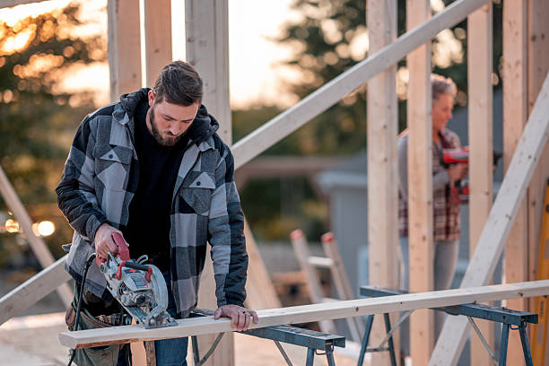 istock Focused Builder Cutting Lumber On Construction Site With Partner In Background At Sunset 2242470974