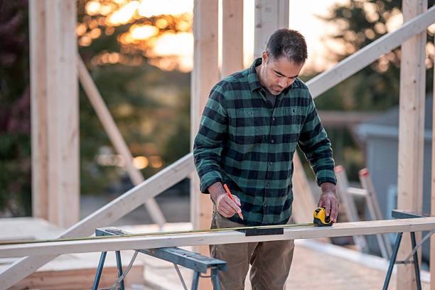 istock Middle-Aged Construction Worker Measuring Wooden Frame at Sunset on Outdoor Build Site 2242470979