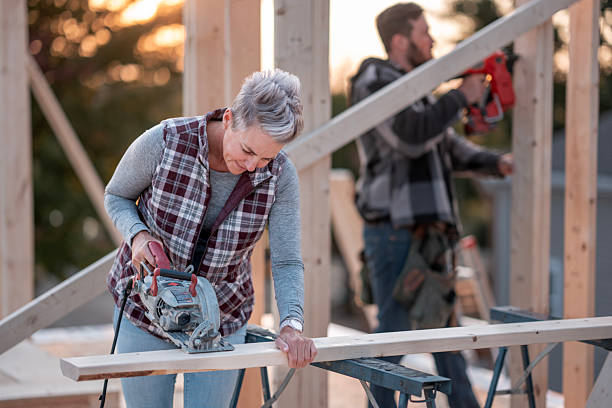 istock Older Woman Using Circular Saw On Wood Beam At Construction Site With Helper In Background 2242470990