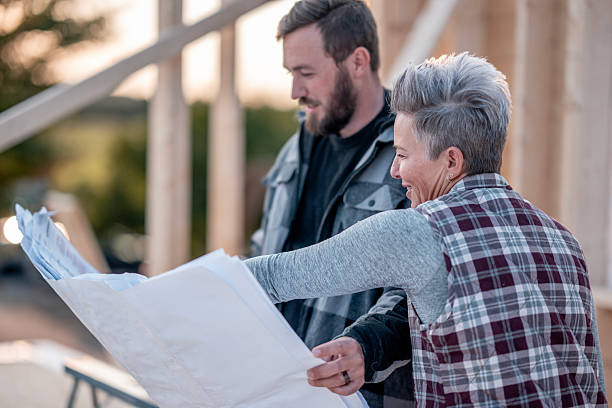 istock Older Woman and Younger Man Reviewing Blueprints Outdoors on Construction Site 2242471042