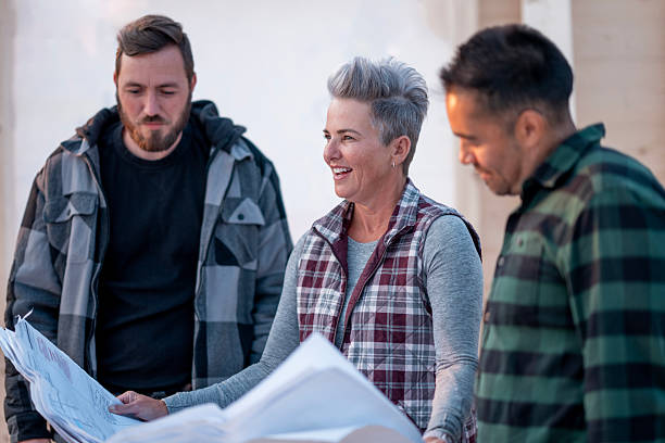 istock Three People Discussing Plans Outdoors, Woman Leading With Blueprints and Colleagues Smiling Together 2242475950