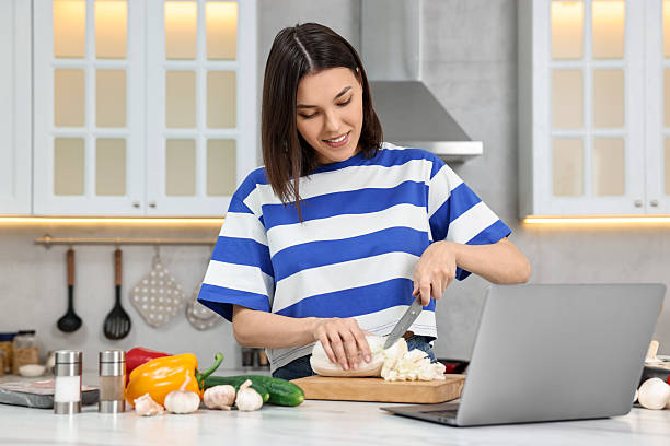 istock Young woman cooking while watching online course via laptop in kitchen 2242478293