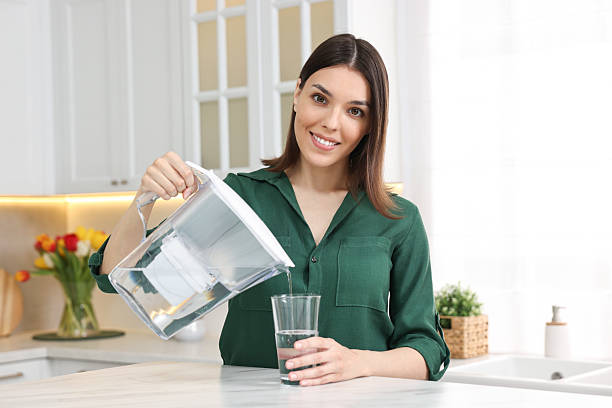istock Woman pouring water from filter jug into glass in kitchen 2242478366