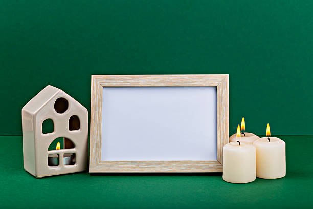 istock Decorative candle arrangement with empty photo frame and ceramic house on green background 2242478643
