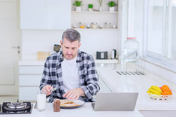istock Middle-aged Man Eating a Simple Breakfast and Working on a Laptop in a Bright Modern Kitchen 2242481489