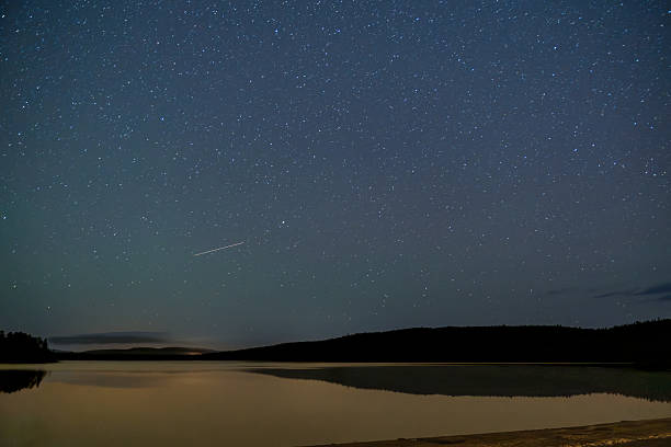 istock Star-filled sky over calm lake and forest horizon under dark night. 2242482637
