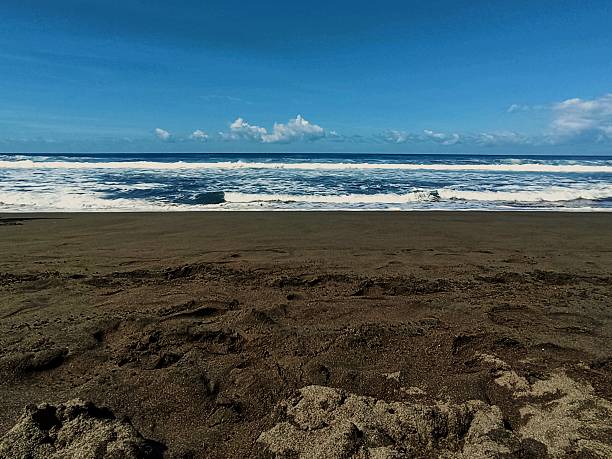 istock Ocean Waves Breaking on Dark Sand Beach Under Blue Sky 2242483340