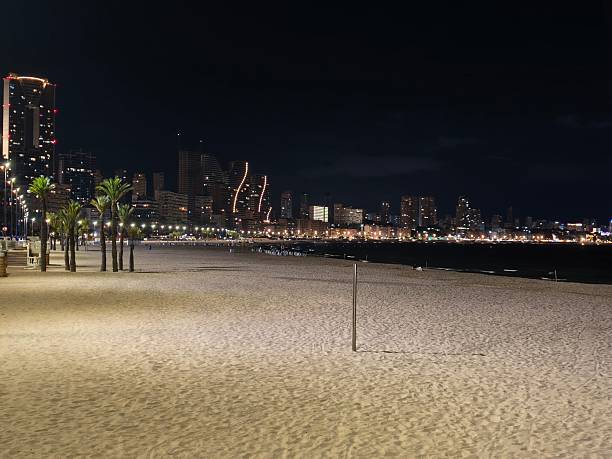 istock beach night lighting, single light pole illuminating vast beach area against city skyline at night 2242489635