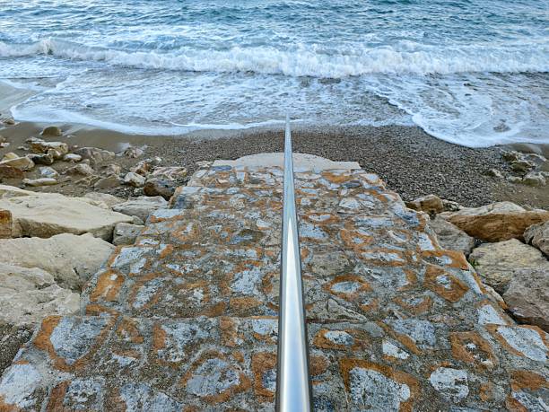 coastal access features, stone stairs and metal railing leading to shoreline with incoming tide