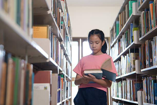 istock A elementary school girl is reading and select a book in the library. 2242497798