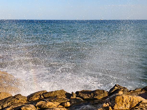 sea mist and gentle waves, serene rocky shoreline with foam and soothing sunlight reflection