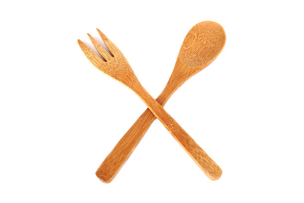 A pair of bamboo kitchen utensils, a fork and a spoon, crossed together on a white background. Eco-friendly, natural texture, and sustainable concept for organic cooking and minimalist lifestyle themes.