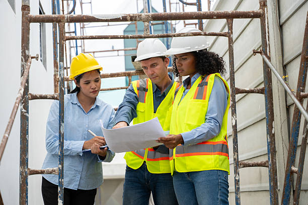 istock Engineers architects wearing safety vests helmets inspect construction site examining building structures discussing project blueprints and tablet construction management, and safety industrial environment. 2242502202
