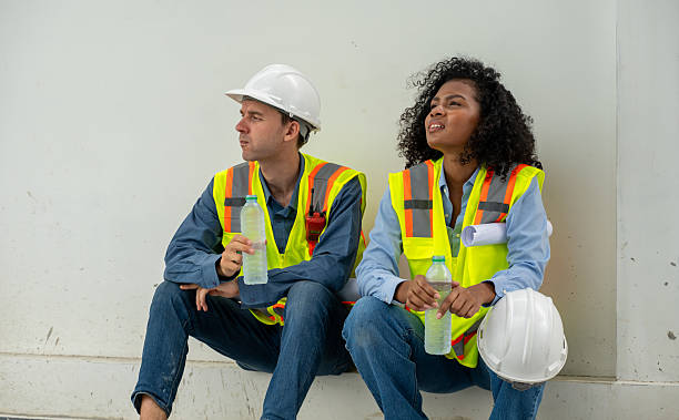 Engineer wearing a safety vest and holding construction plans takes a break and a water bottle, appearing thoughtful rest during a workday construction or engineering field
