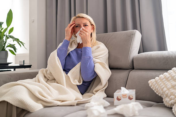 istock Sick woman with headache and cold sitting on couch 2242502951