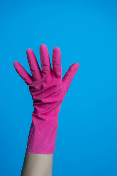 A close-up of a raised hand wearing a bright pink cleaning glove against a vivid blue background.