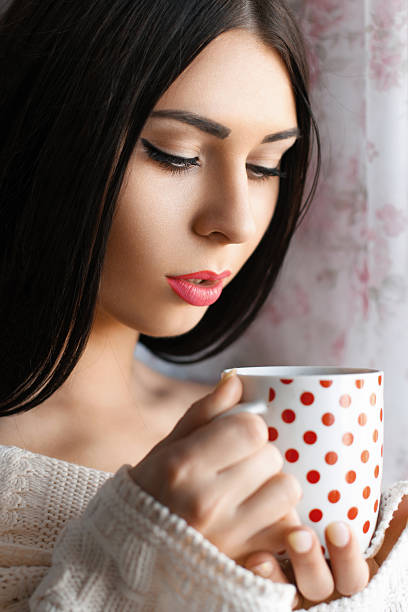 istock Beautiful girl drinking coffee by the window 2242506910