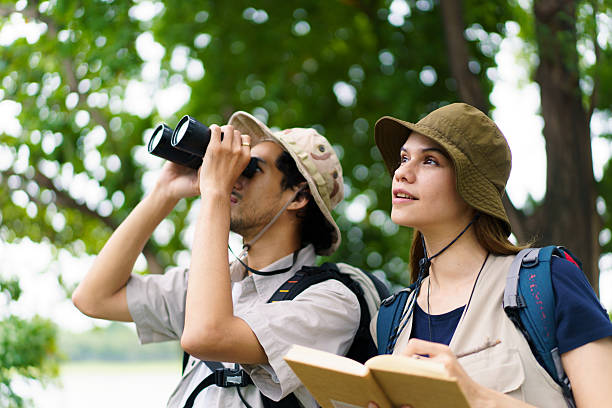 Asian man and woman hikers with binoculars birdwatching and taking notes in nature