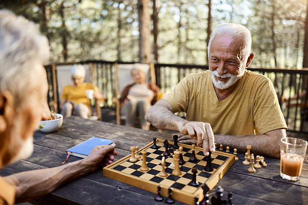 Happy mature men talking while playing chess on a terrace. Women are in the background.
