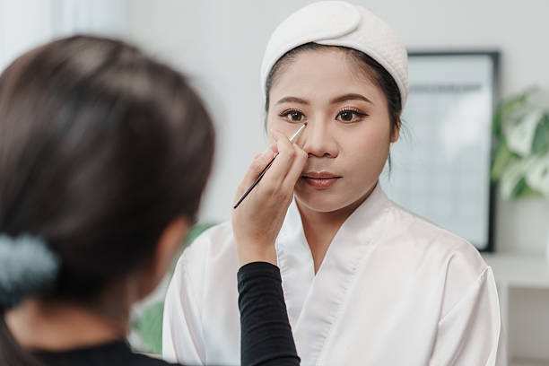 Asian bride getting eyeshadow blended by beautician make-up artist preparation for wedding day. Applying cosmetics. make-up artist working make up on female client in studio workplace.