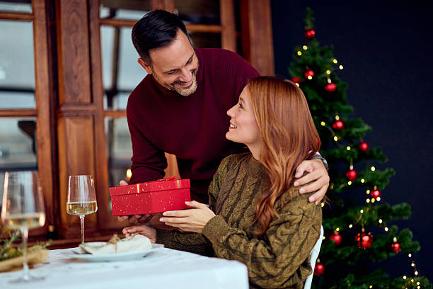 Couple Celebrating Christmas With Gift Exchange At Home Near Decorated Christmas Tree stock photo