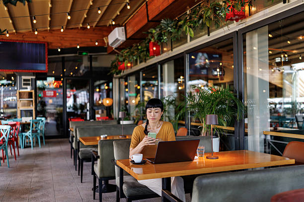 istock Beautiful Japanese woman using smart phone while working on her laptop in a contemporary coffee shop 2242525439
