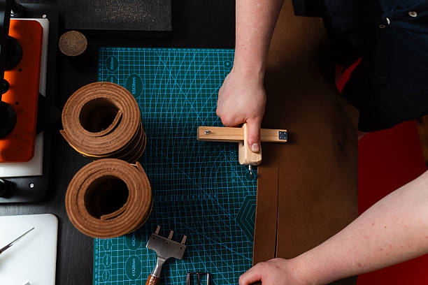 istock Craftsman preparing leather strap using wooden cutter on mat. Handmade leather belt preparation with wooden strap cutter on cutting mat. Artisan is cutting leather strip with wooden tool. 2242525874