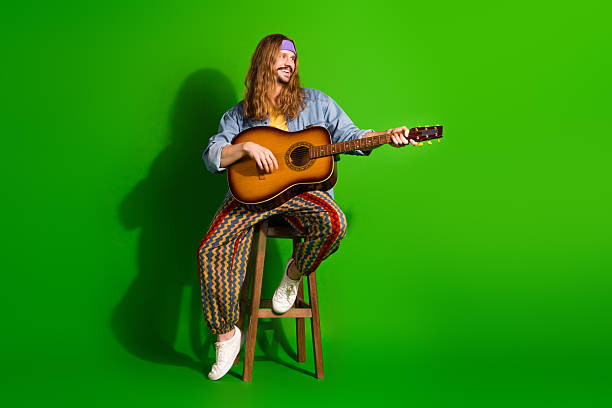 istock Young man with relaxed demeanor playing an acoustic guitar while sitting against a vibrant green background 2242526317