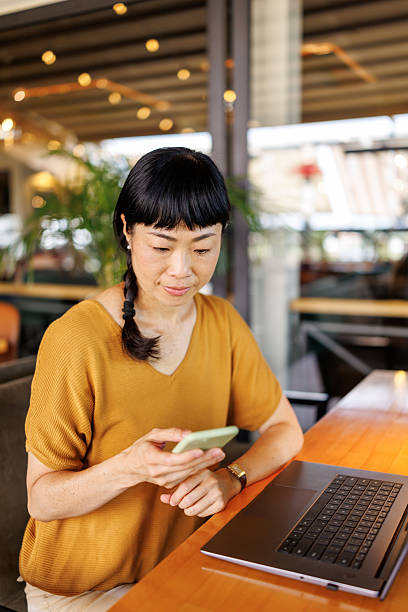 istock Beautiful Japanese woman using smart phone while working on her laptop in a contemporary coffee shop 2242526643