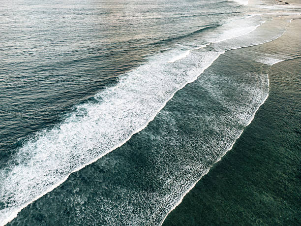 Aerial view of tropical Bali coast with turquoise waves breaking into white foam on shallow sandy seabed, serene seascape texture