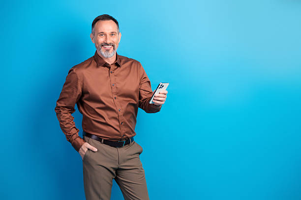 istock Confident mature businessman smiles while using smartphone against bright blue background for a modern corporate lifestyle stock photo 2242531272