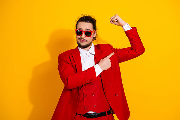 istock Funny stylish man in red suit posing with flexing arm against bright yellow background for bold fashion ad 2242531718