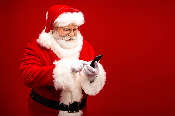 istock Santa Claus using smartphone in bright red studio posing for Christmas themed stock image 2242534964